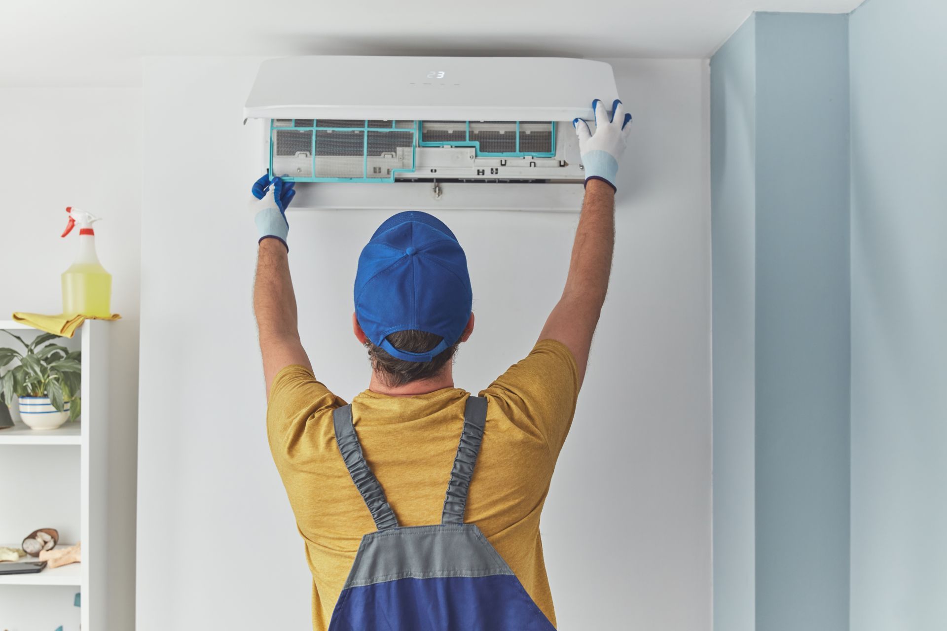 Technician installing a wall-mounted air conditioner indoors with tools raised overhead