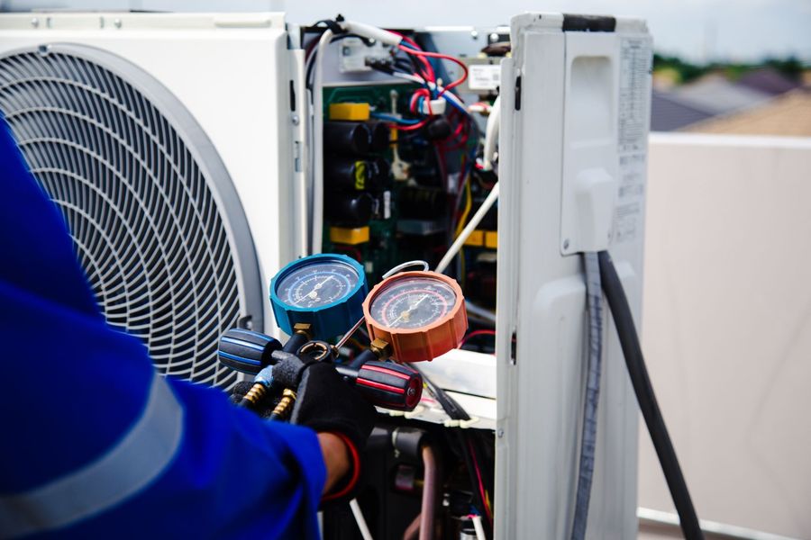 Technician using gauges to service an outdoor air conditioner unit with exposed wiring