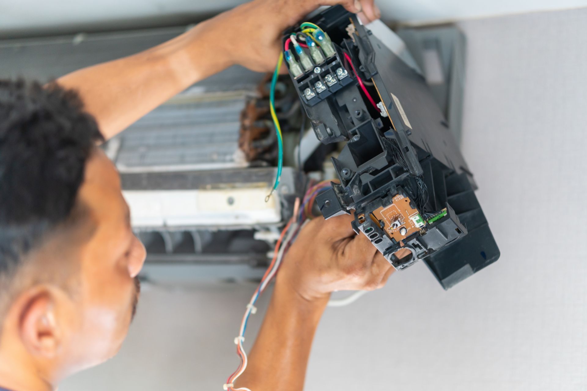 Technician installing a wall-mounted air conditioner, holding the unit open to expose wiring and components