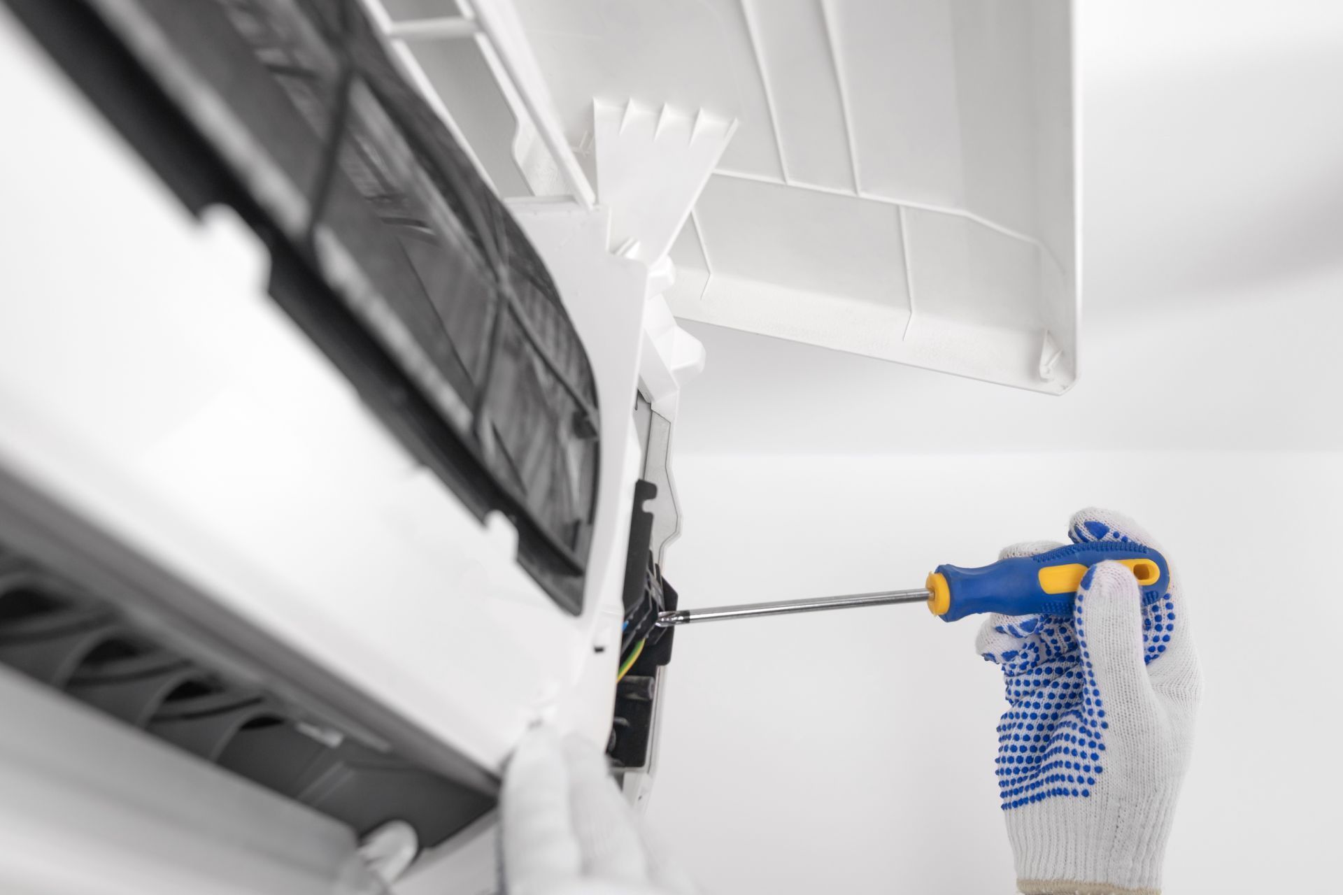 Person using a blue drill to install a white ceiling fixture indoors