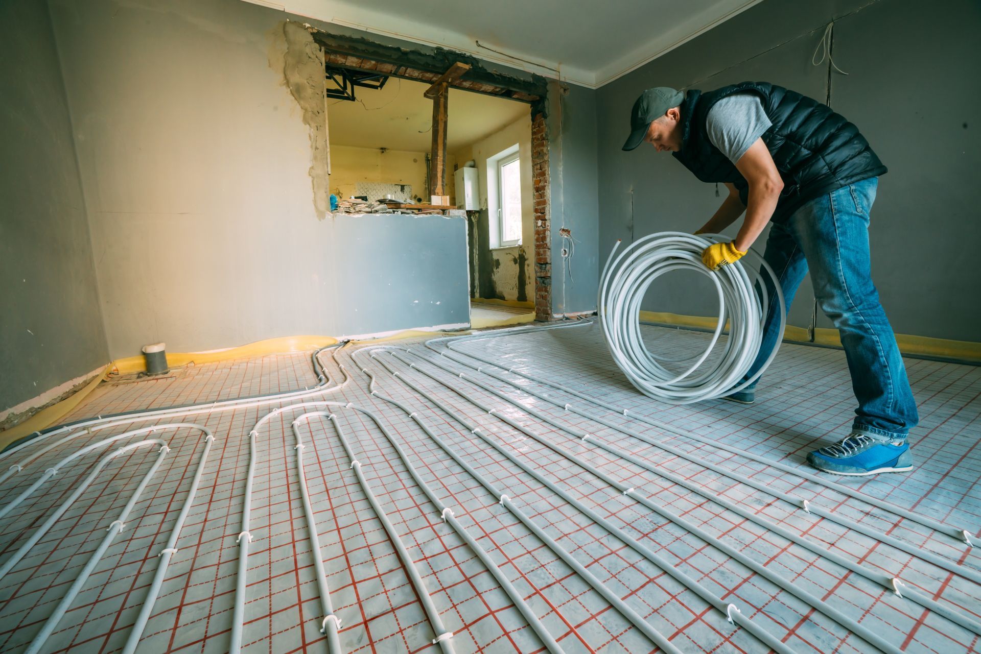 Worker installing underfloor heating pipes in a room during renovation