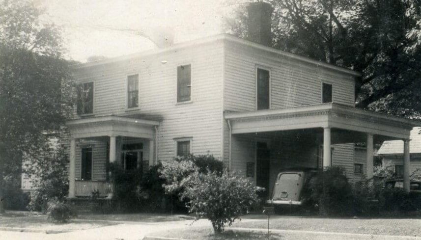 Two-story white house with covered porch and car parked in front.