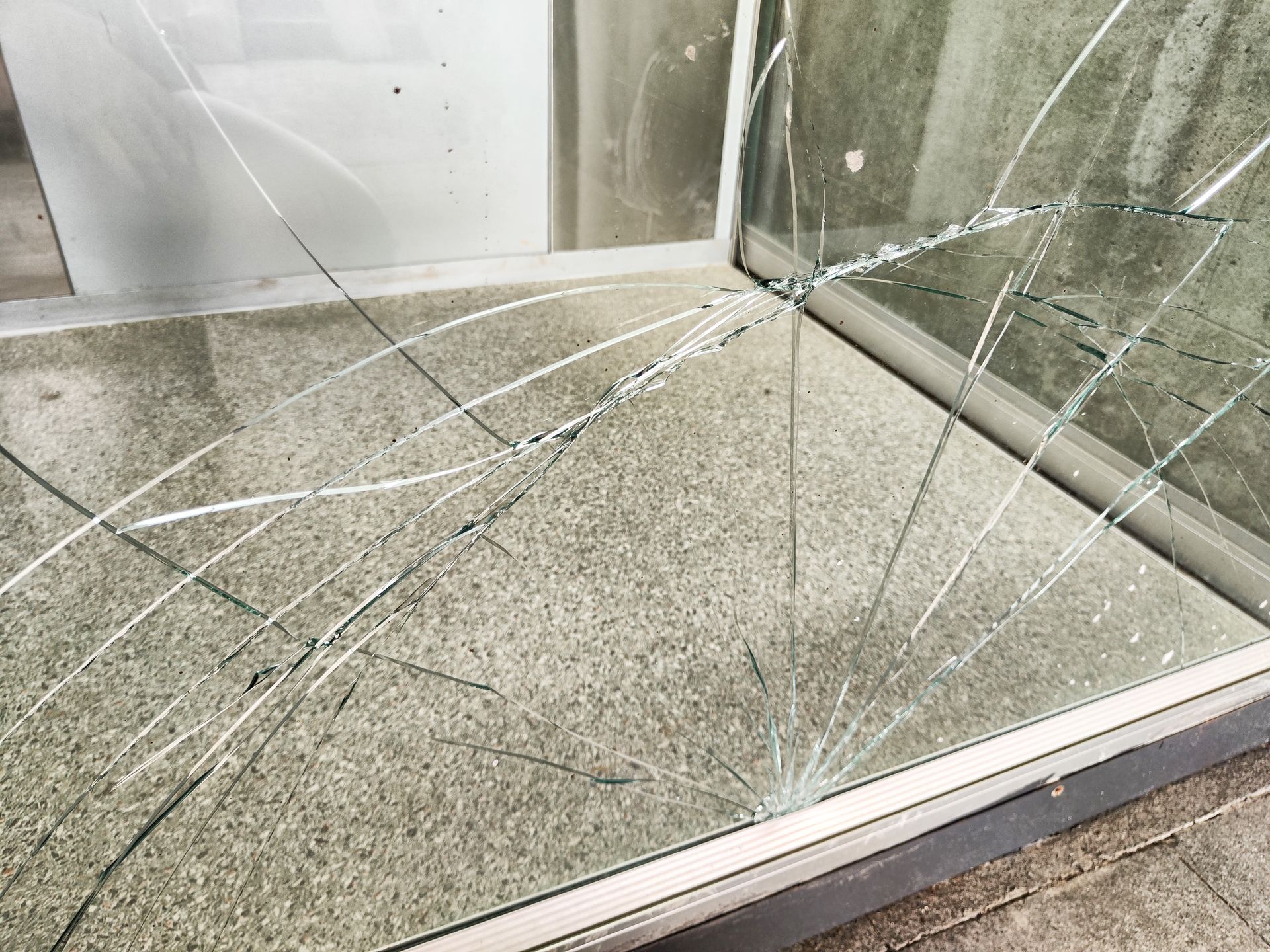 Shattered glass window, with cracks radiating from a central impact point, resting in a metal frame.