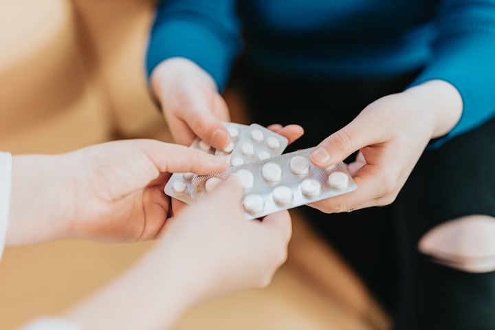 Person's hands holding blister packs of white pills, passing them to another person.