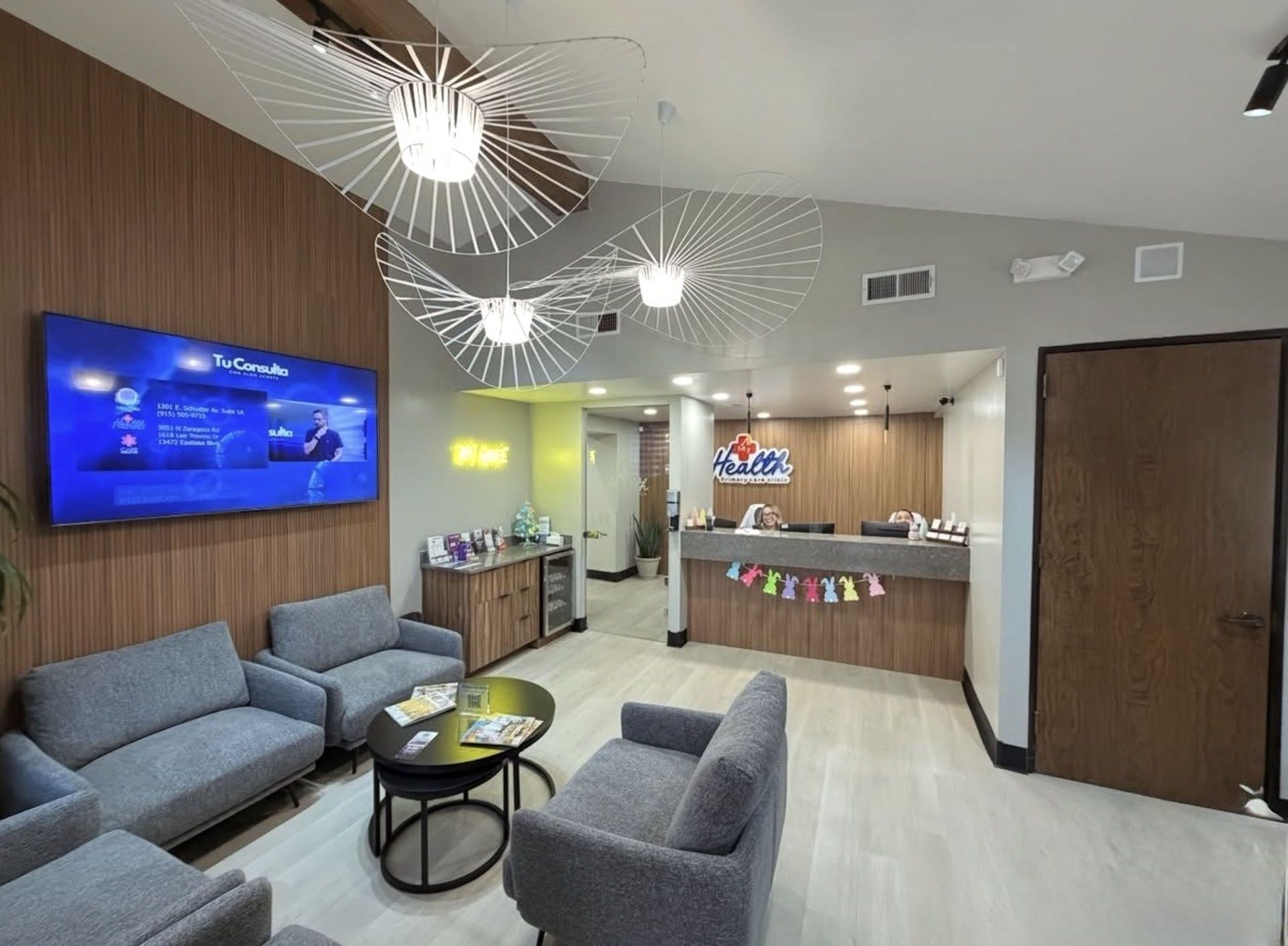 Modern waiting room with gray chairs, wall TV, pendant lights, and a reception desk in El Paso TX