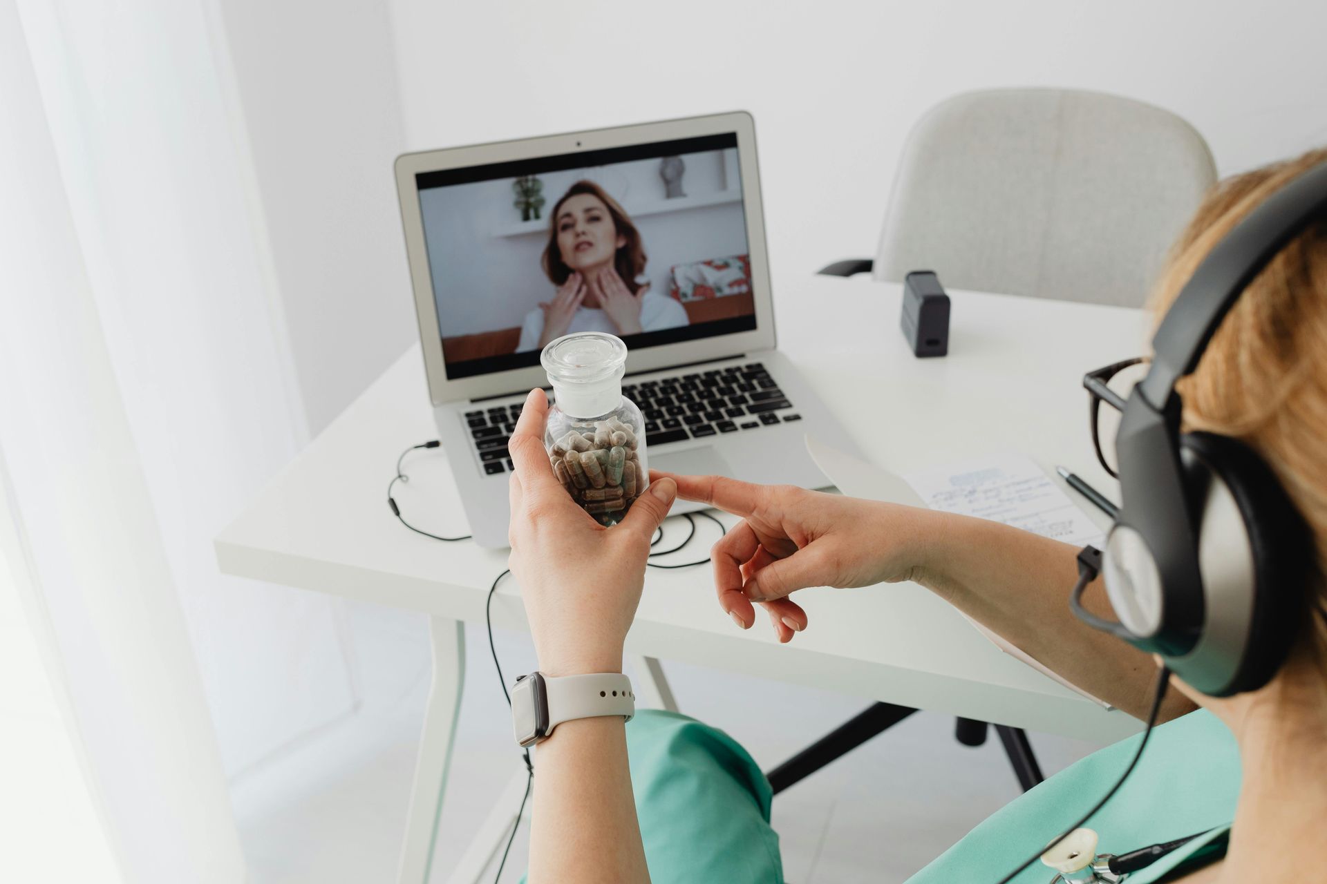 Person on video call holding a jar of capsules, consulting with a person on laptop screen.