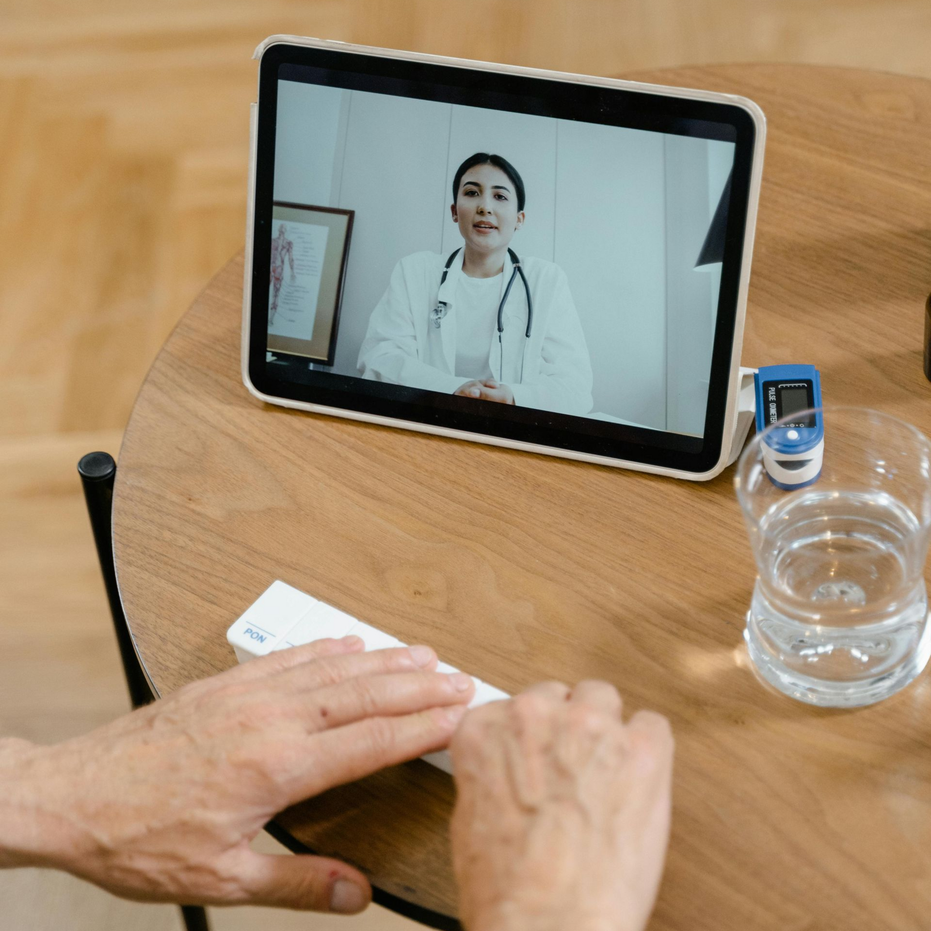 Person having a telehealth visit with a doctor on a tablet. Table with oximeter, test kit, and glass of water.