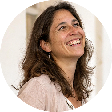 Woman smiling, looking upward. Brown hair, wearing a light pink jacket, indoors, natural light.