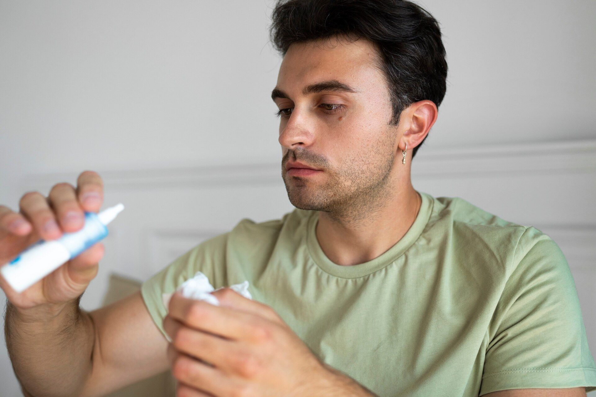 Man squeezing ointment from a tube onto a tissue. He has a concerned expression, indoors.