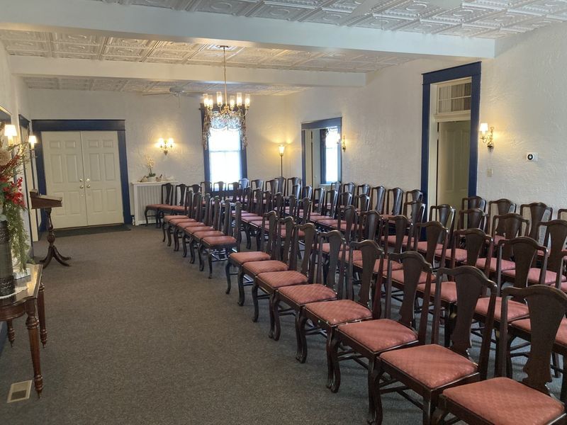 Interior of a room with rows of chairs, likely for a ceremony, with ornate ceiling and wall details.