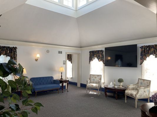 A light-filled room with a blue sofa, two patterned armchairs, and a large TV.
