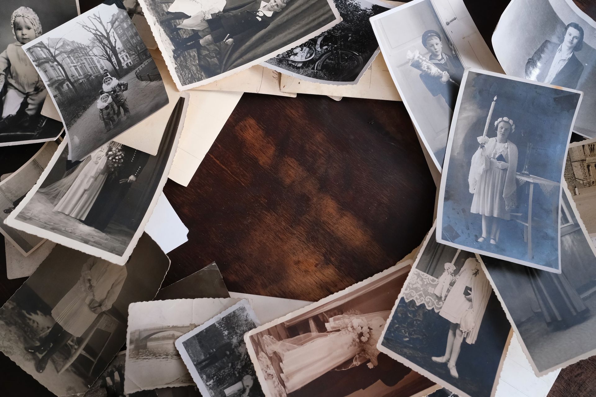 Pile of vintage black and white photographs on a wooden surface.