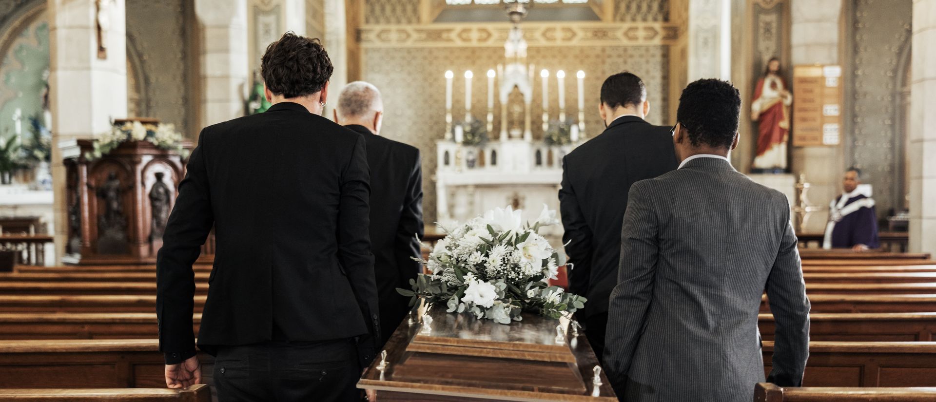 Four men carrying a coffin down the aisle of a church during a funeral.