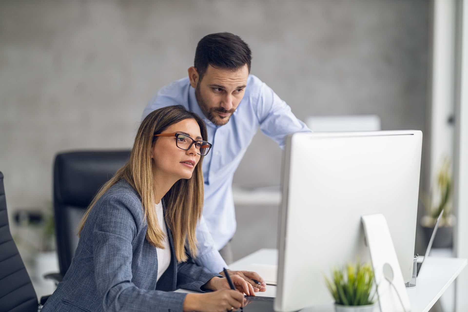 Woman and man looking at a computer screen in an office. The man is leaning over her shoulder.