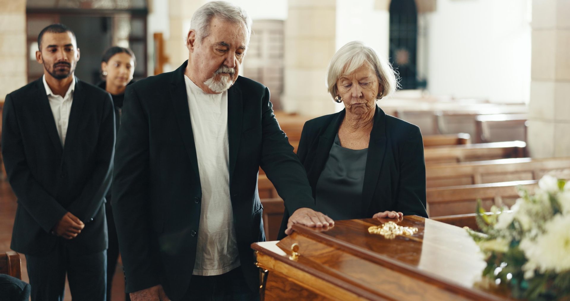 People at a funeral, looking at a closed casket. The setting is a church, somber.