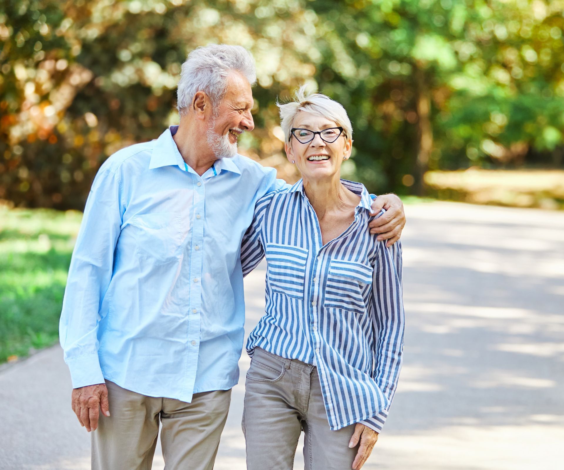 Smiling older couple walking outdoors; man has arm around woman.