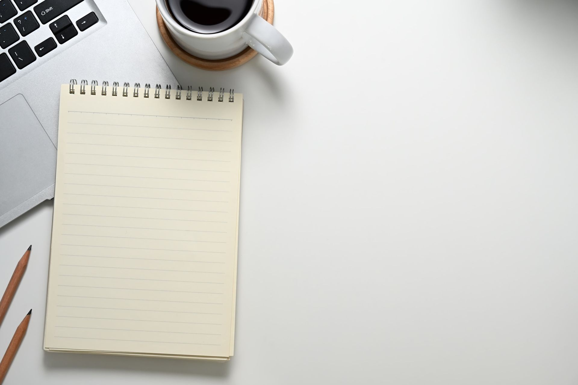Laptop, notepad, coffee cup, and pencils on a white desk.