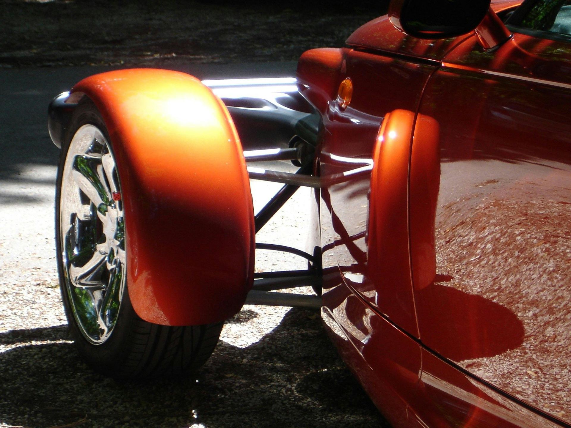 A red car with a chrome wheel is parked on the side of the road
