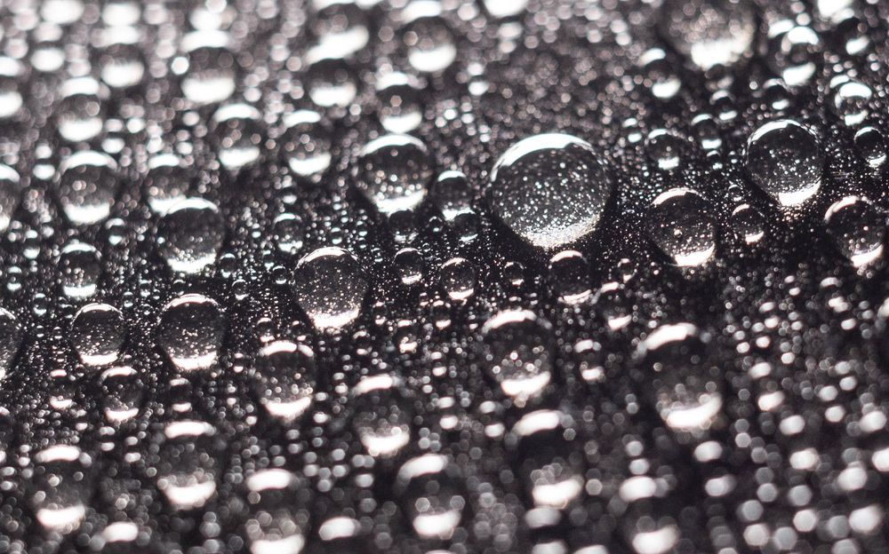 A close up of water drops on a black surface.
