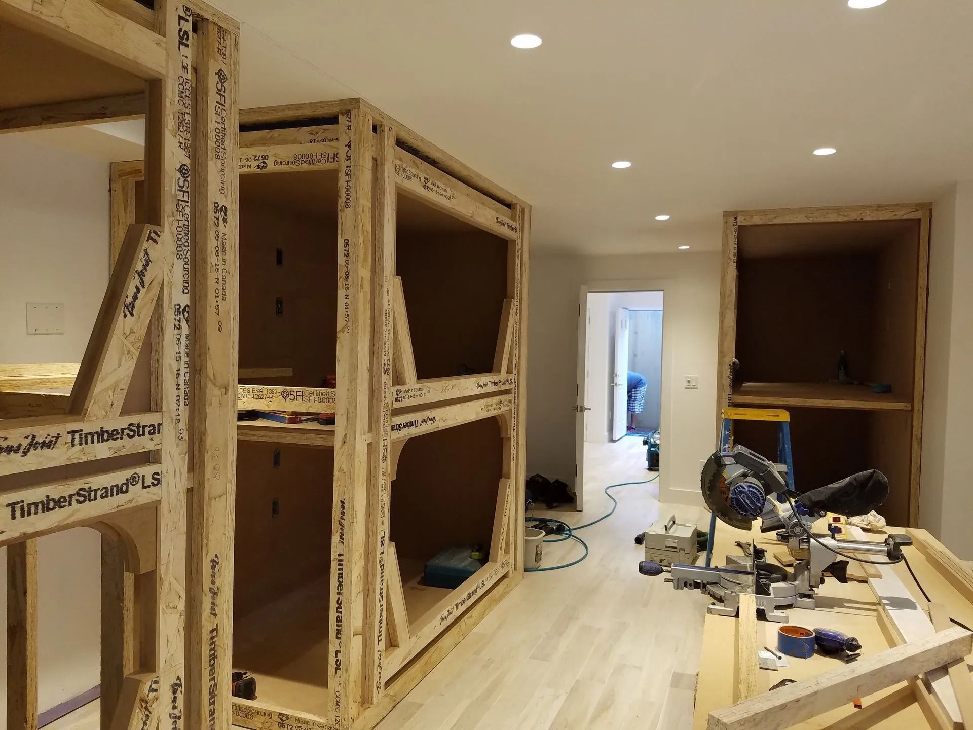 Wood bunk bed frames under construction in a room, with tools and a doorway.