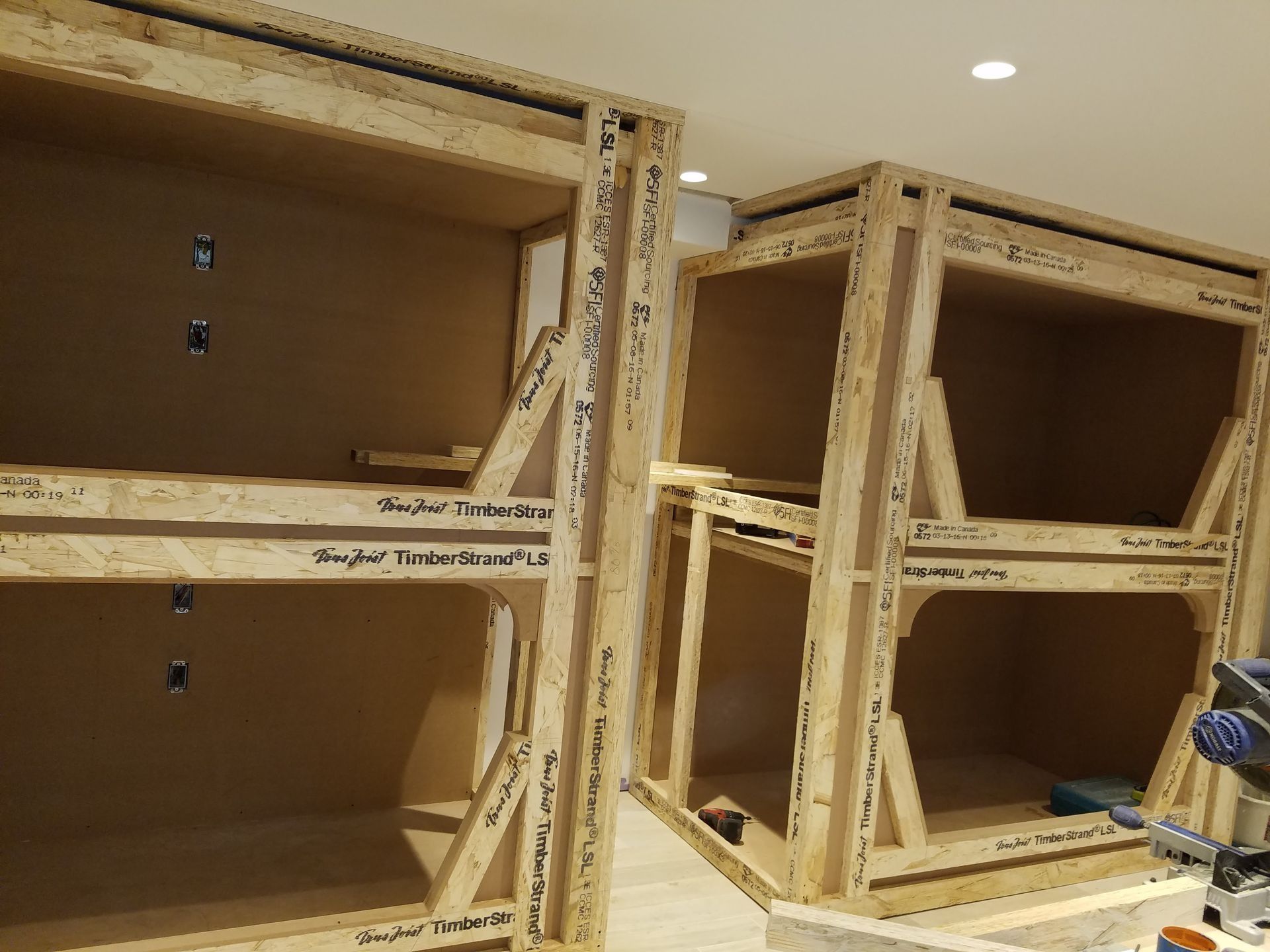 Wooden framework of cabinets under construction, in a light-colored room.