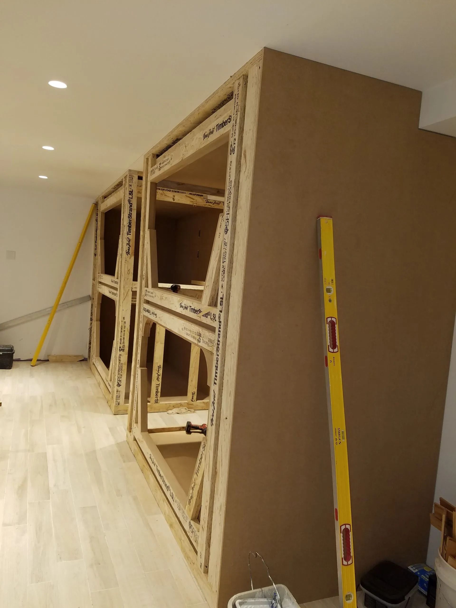 Construction of built-in shelving with wooden frames and large brown panels in a room with hardwood floors.