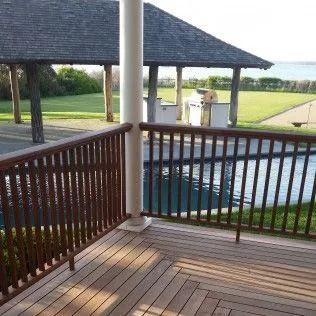Wooden deck with railing overlooking a pool and gazebo near the ocean.