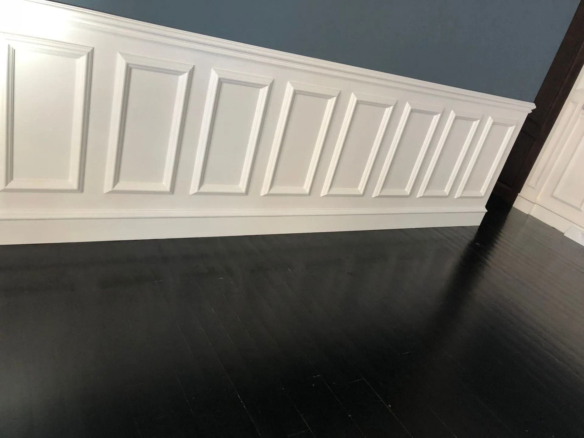 White paneled wall with dark wood floor.