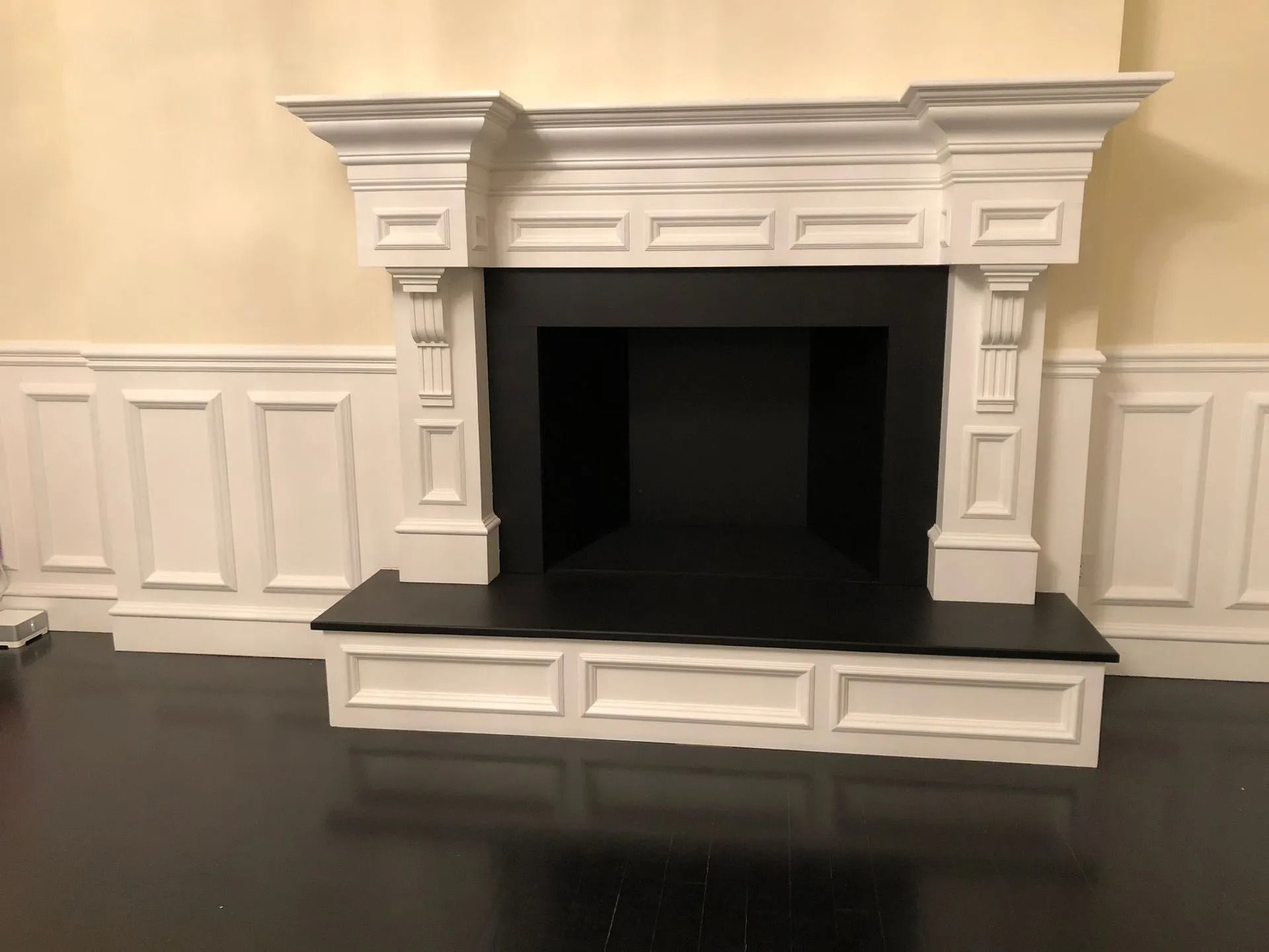 White mantel fireplace with black interior, set against cream walls and dark wood floor.