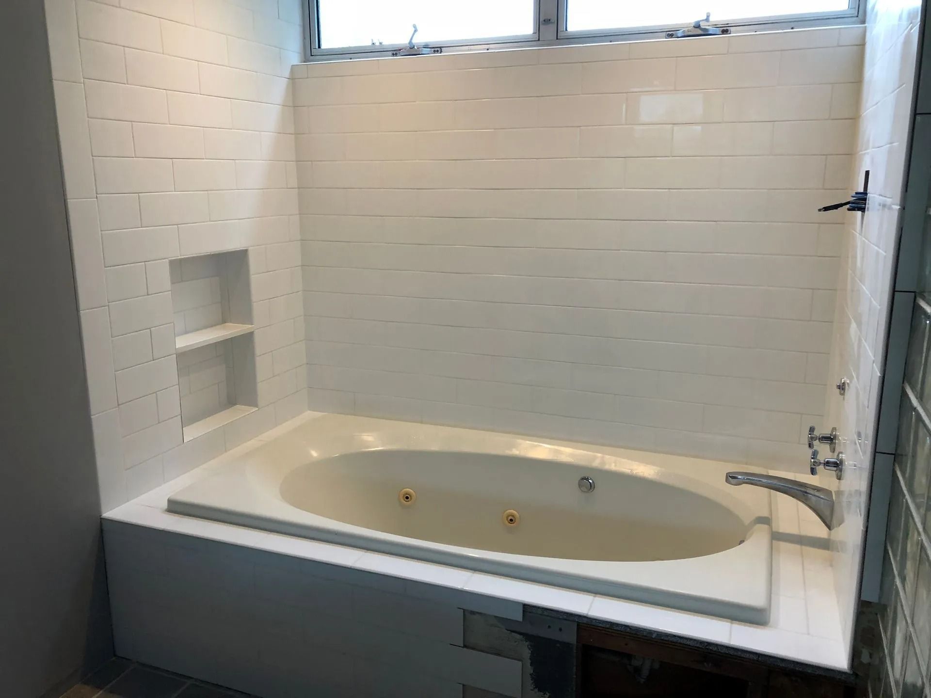 White tiled bathtub with built-in shelves, under a window.