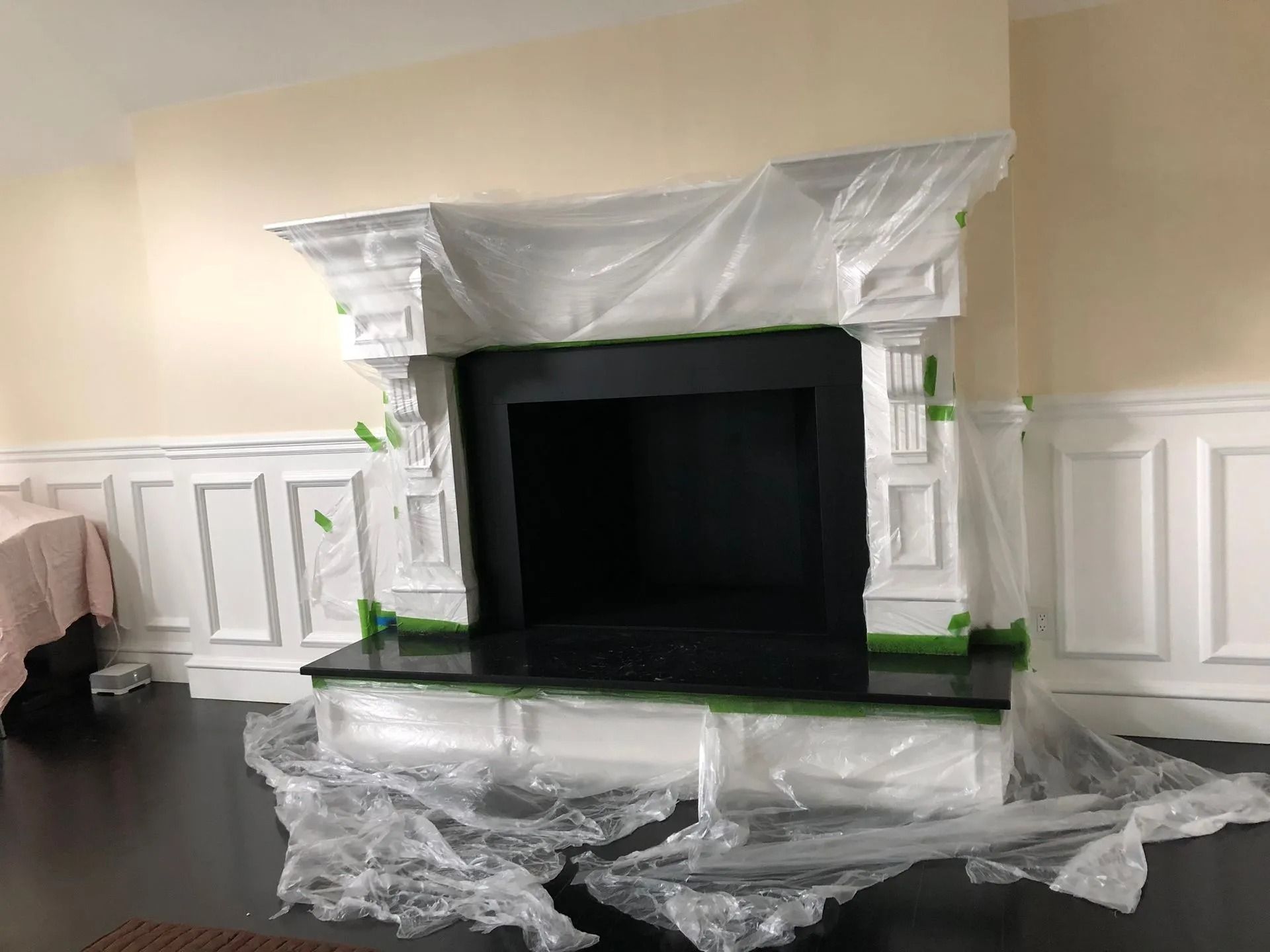 Fireplace with white mantel and black interior, covered in plastic sheeting. Dark hardwood floor.