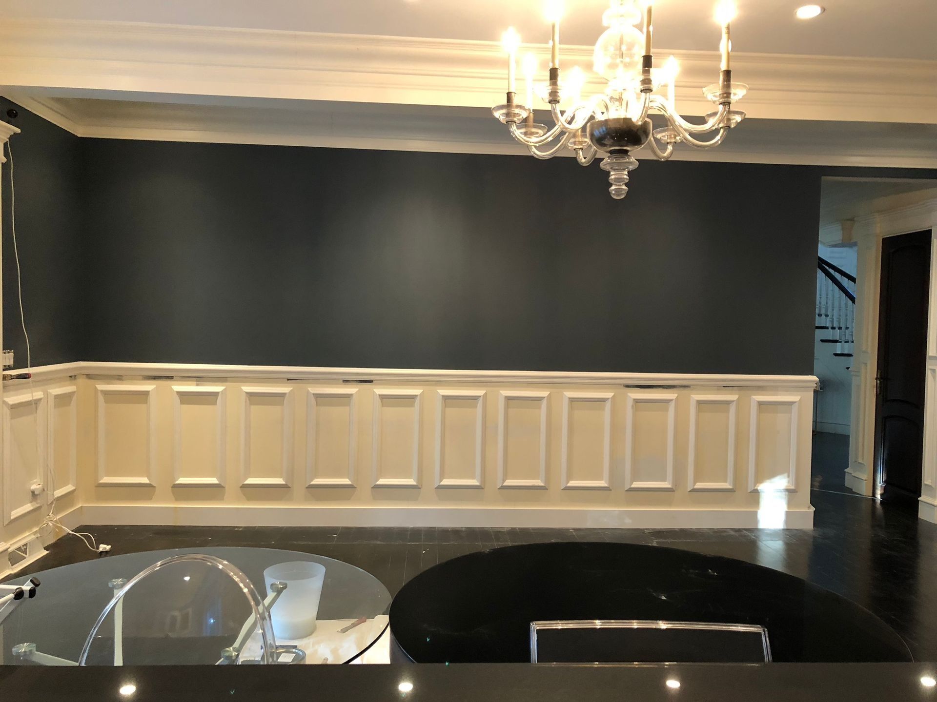 Formal dining room with dark gray wall, white wainscoting, chandelier, and black flooring.
