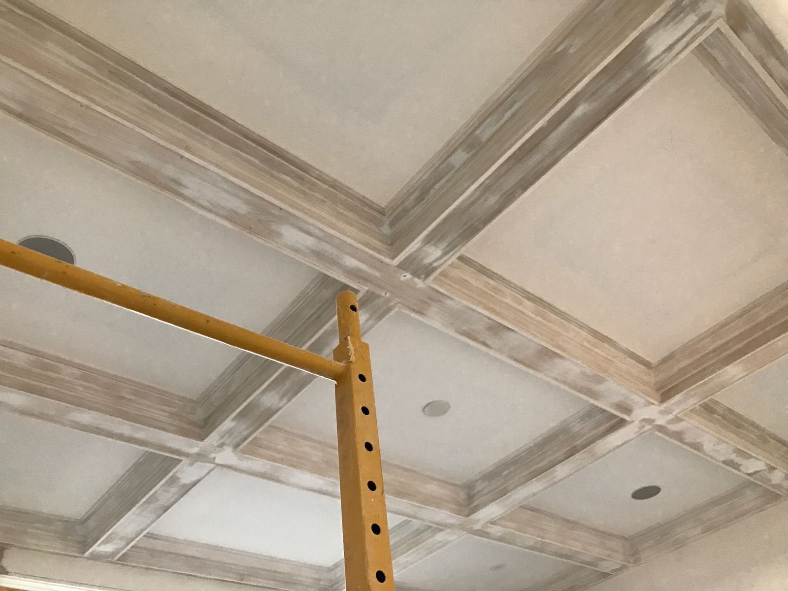 Ceiling with coffered beams; unfinished with light gray and white paint; construction scaffold in view.