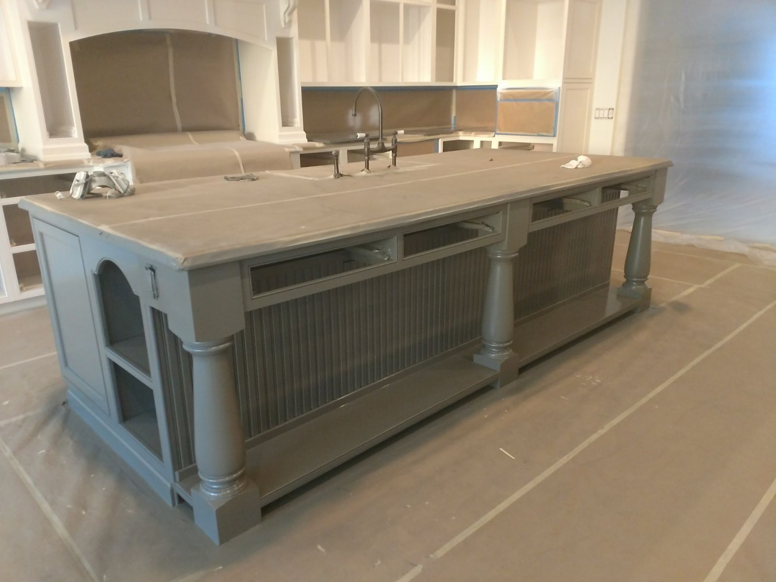 Gray painted kitchen island with decorative columns and open shelving, in a room being renovated.
