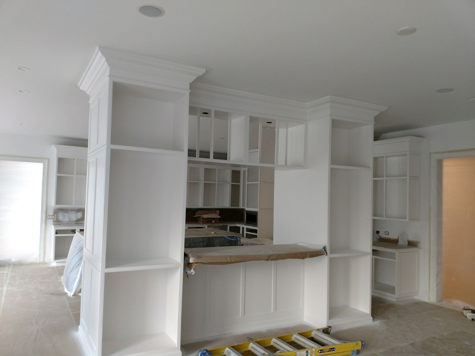 White built-in shelving unit under construction; room with open doorway, ladder, and unfinished walls.