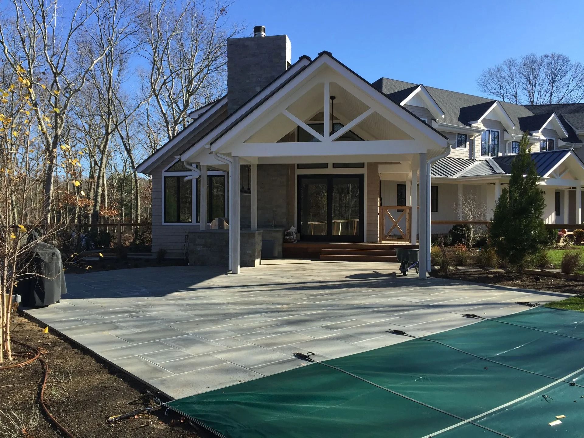 Stone patio with a covered outdoor seating area and a pool in a backyard.