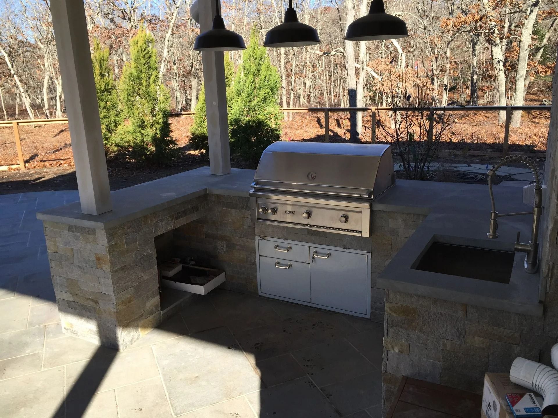 Outdoor kitchen with stainless steel grill, sink, and storage. Stone walls and concrete patio.