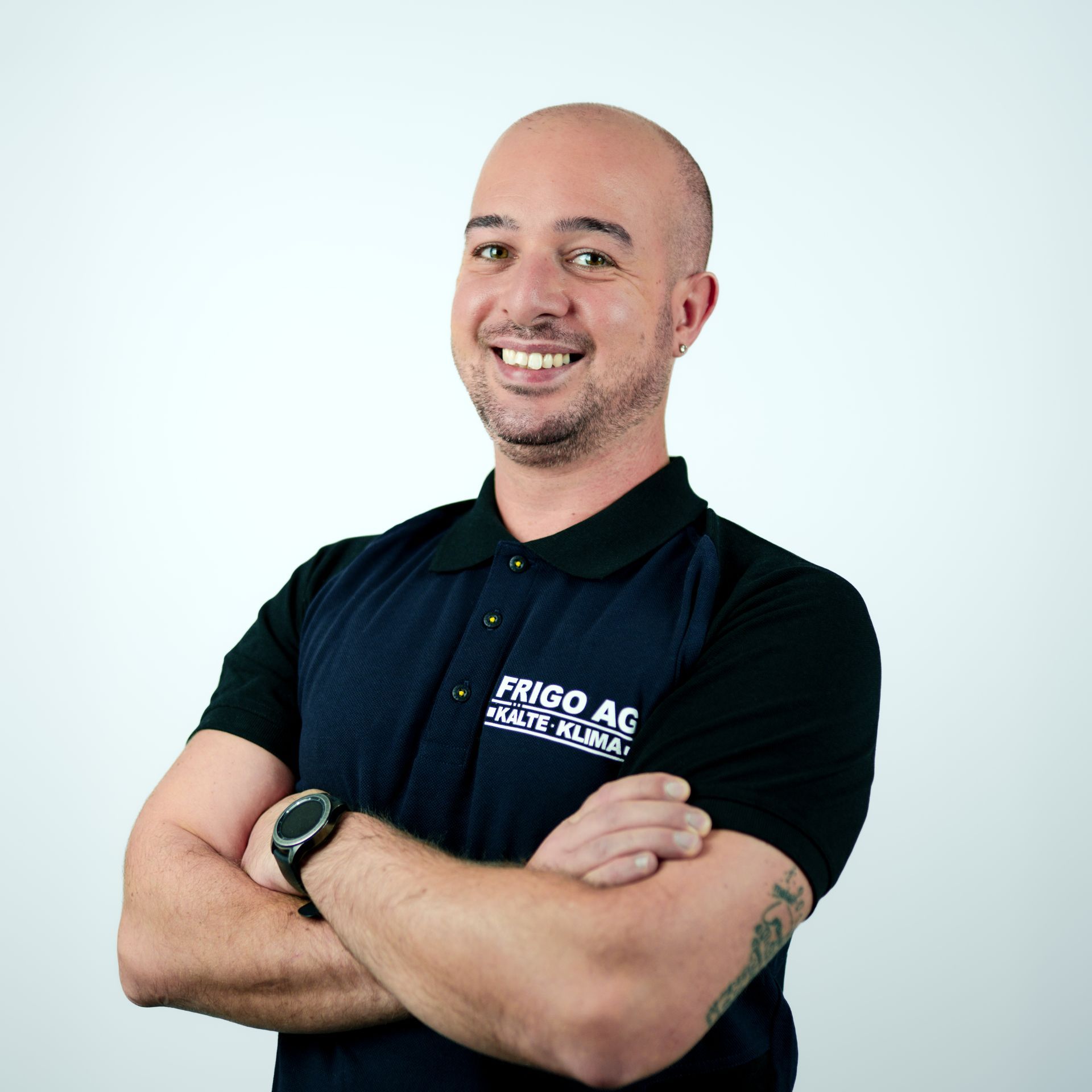 Mann mit verschränkten Armen, lächelnd, bekleidet mit einem schwarz-blauen Poloshirt mit Logo.