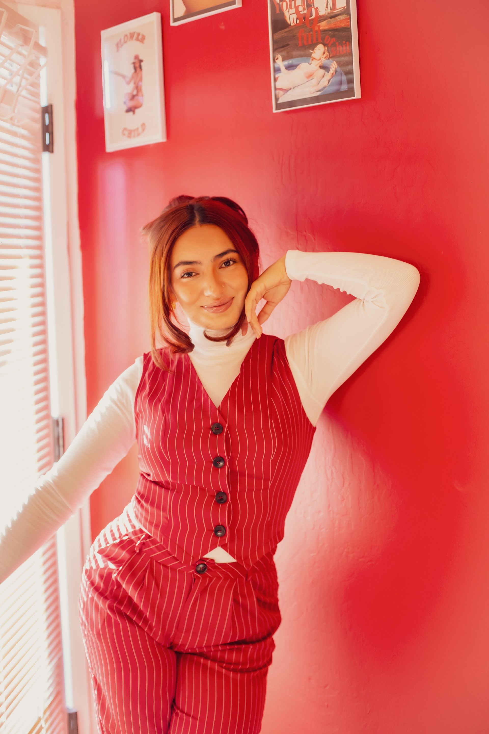 Woman in red pinstripe suit and white turtleneck poses by red wall.
