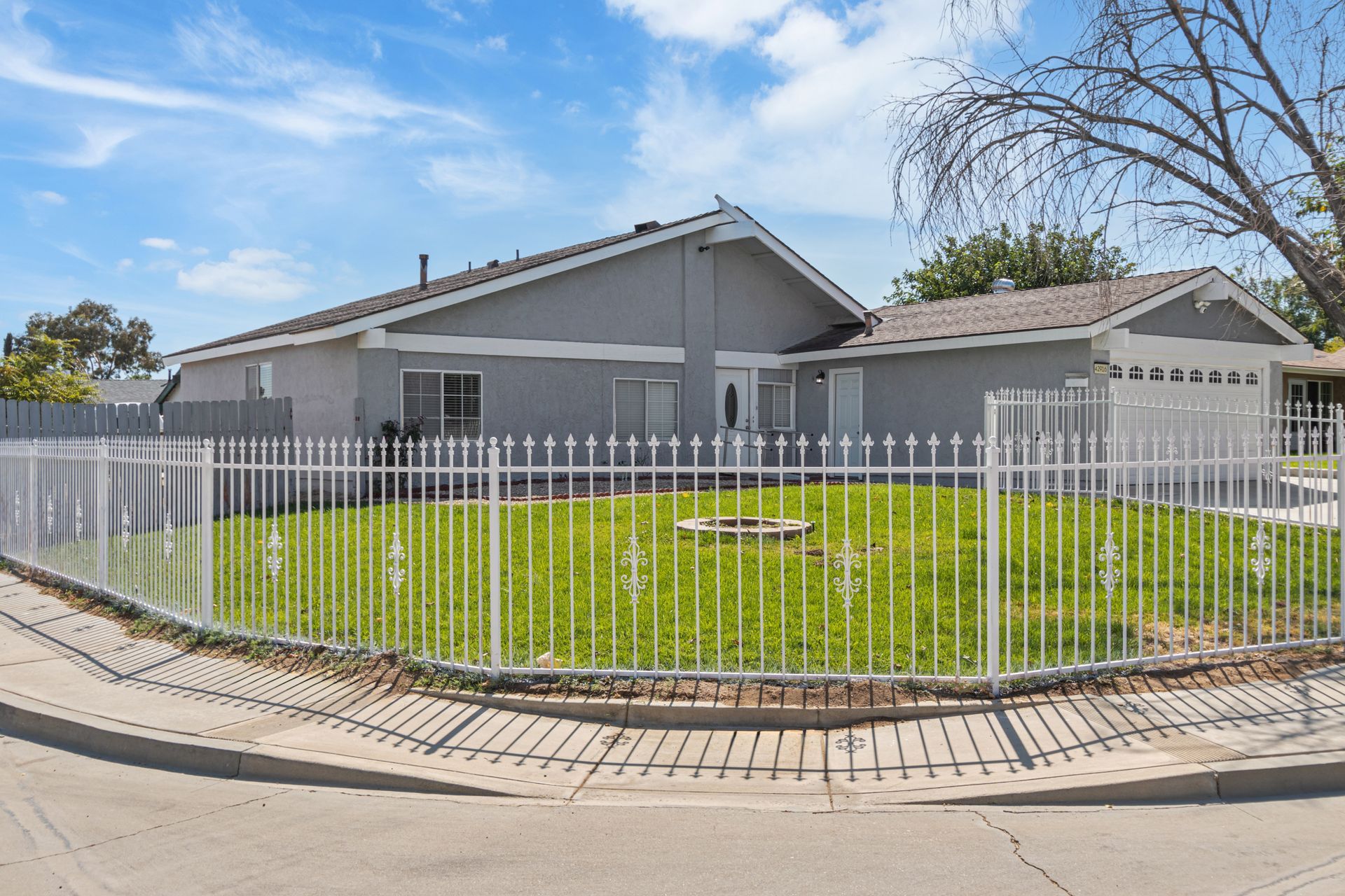 Gray house with white fence and a lawn on a sunny day.
