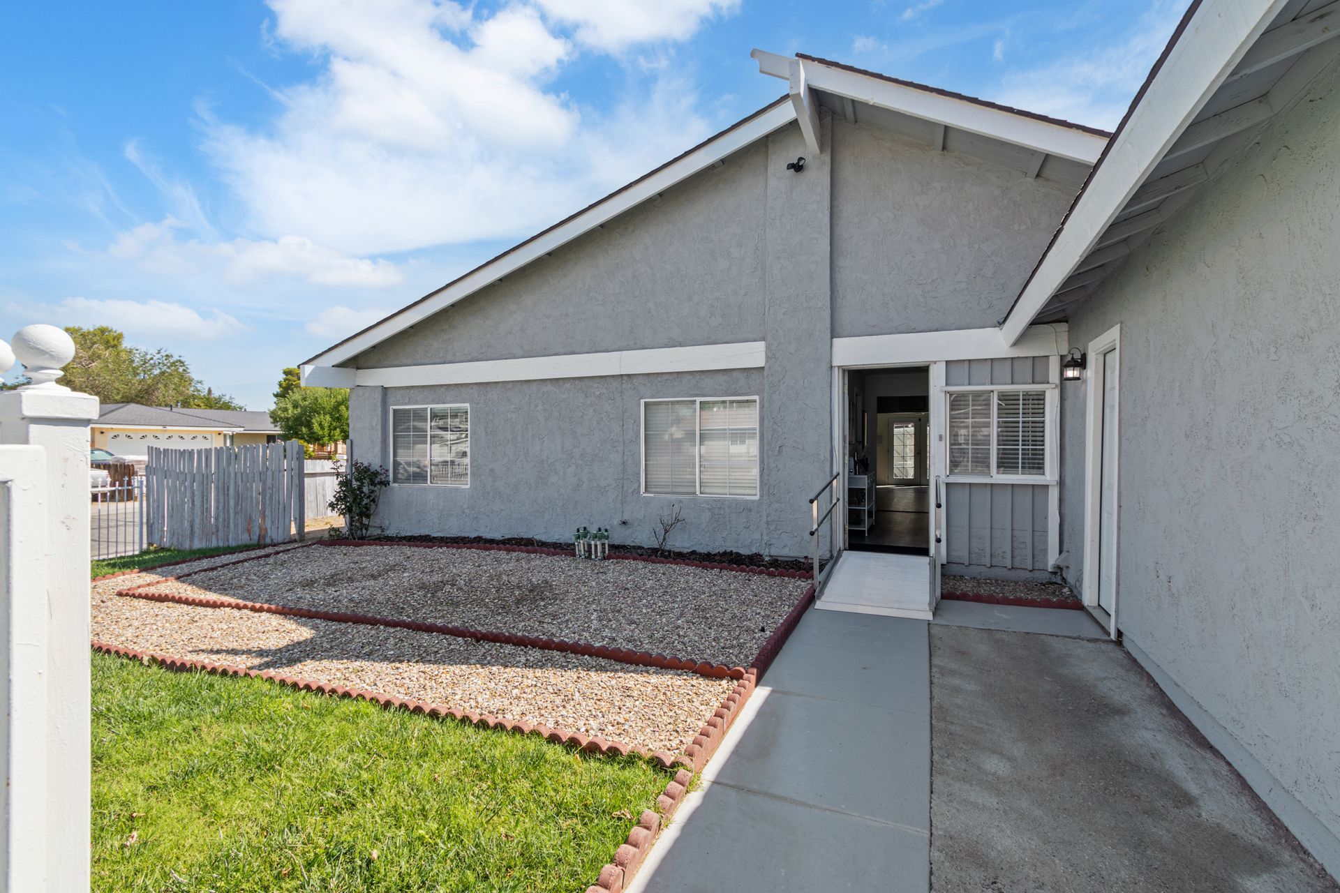 Gray house exterior with a small yard and stone landscaping under a blue sky.