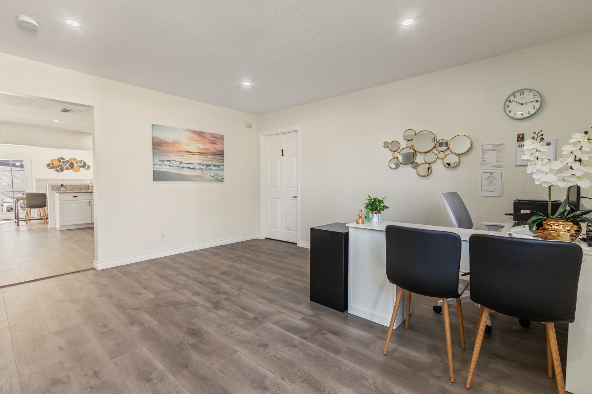 Reception area with a desk, two chairs, a painting, and a clock on the wall.