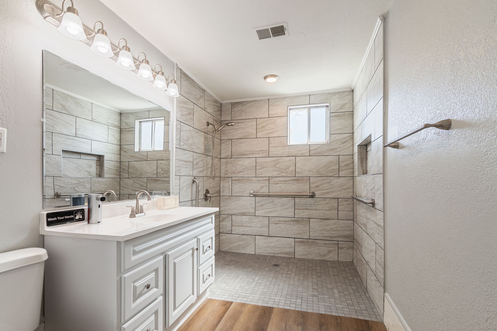 Bathroom with white cabinets, large mirror, tiled shower, and light-colored flooring.