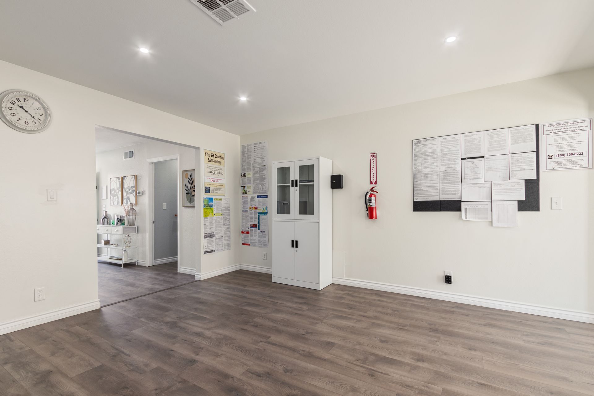 Empty office space with wood-look flooring, white walls, and a doorway leading to another room.