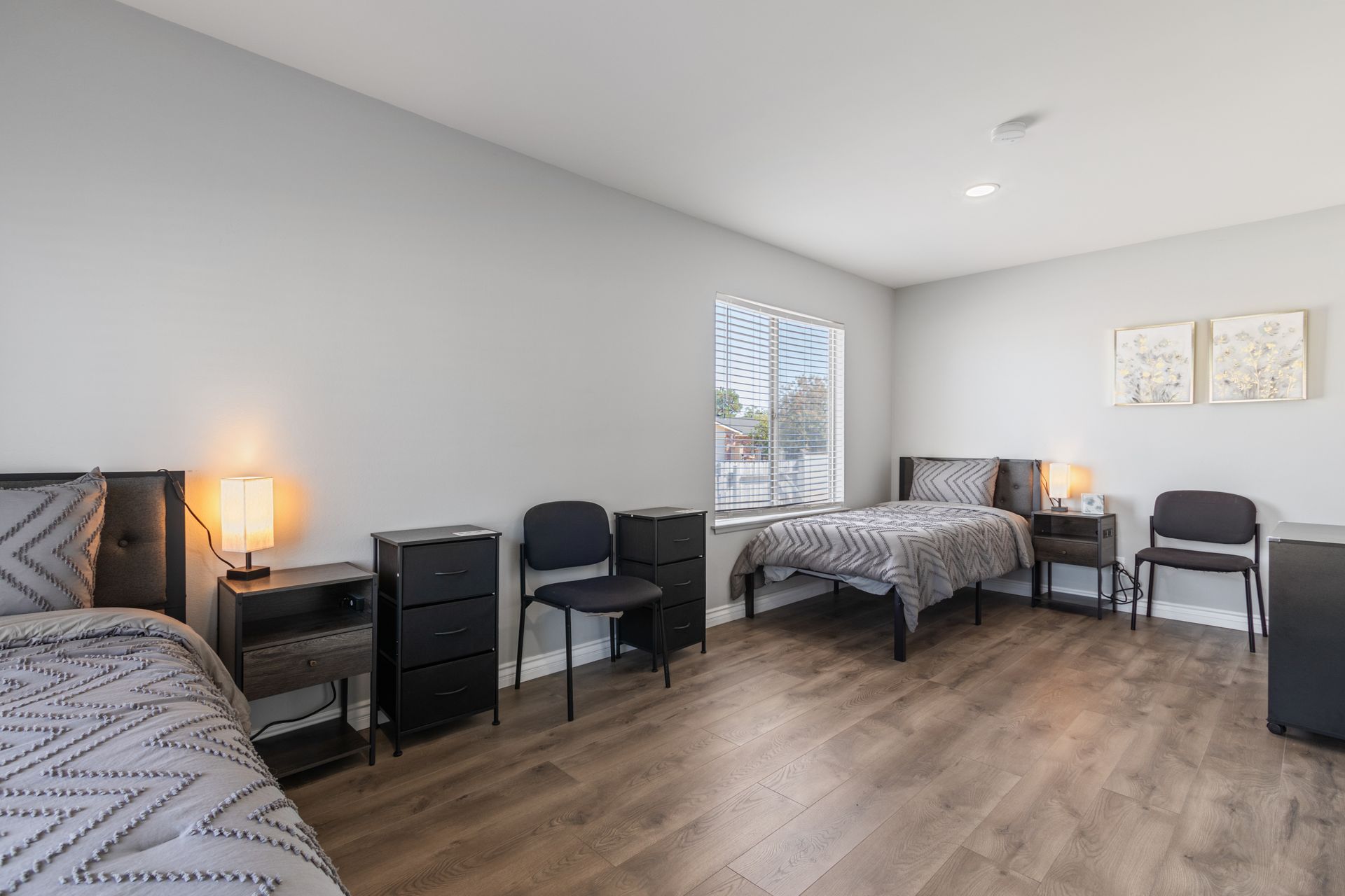 Bedroom with two twin beds, grey walls, black furniture, and a window.