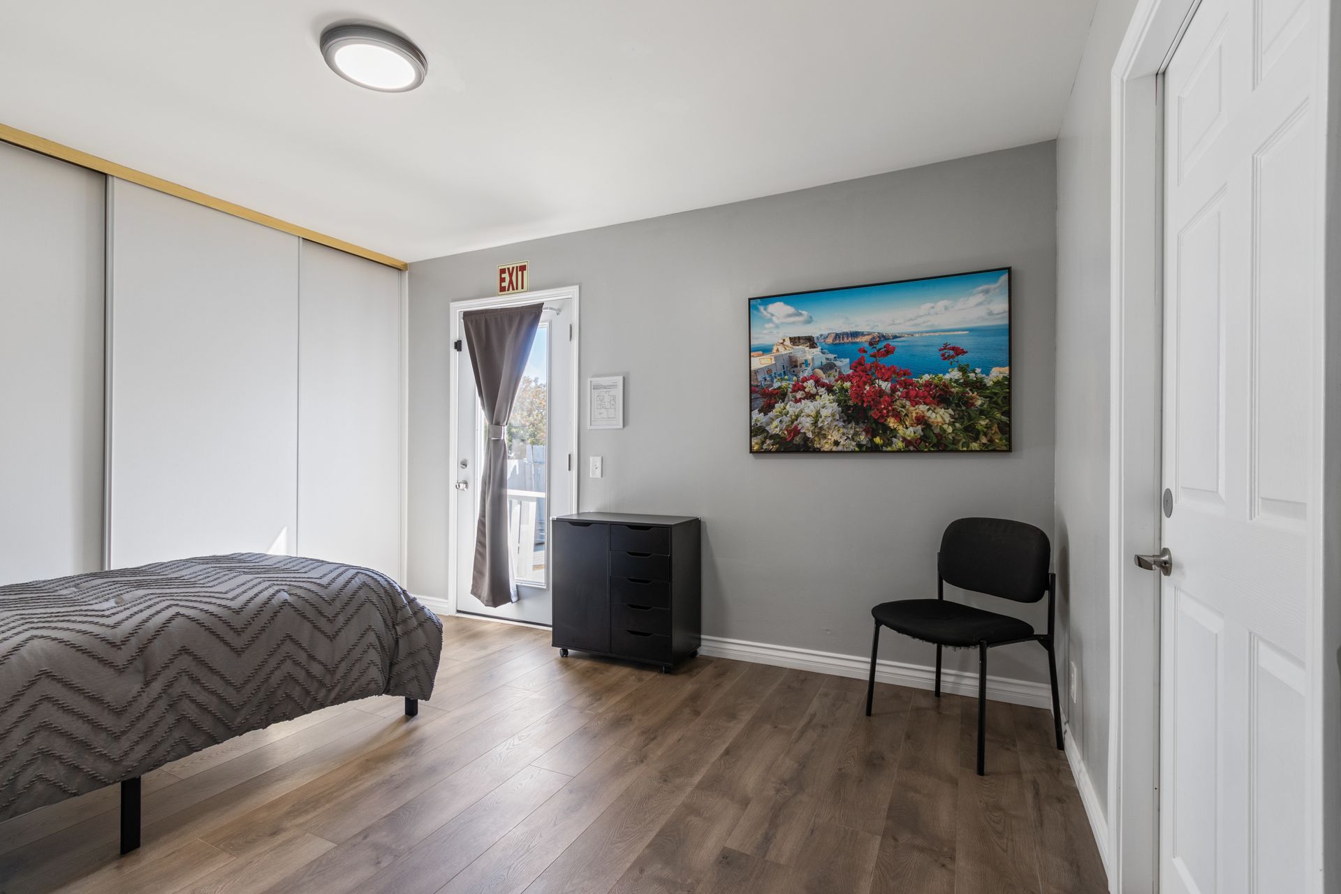 A well-lit room with a massage table, chair, and artwork. Door to the outside.