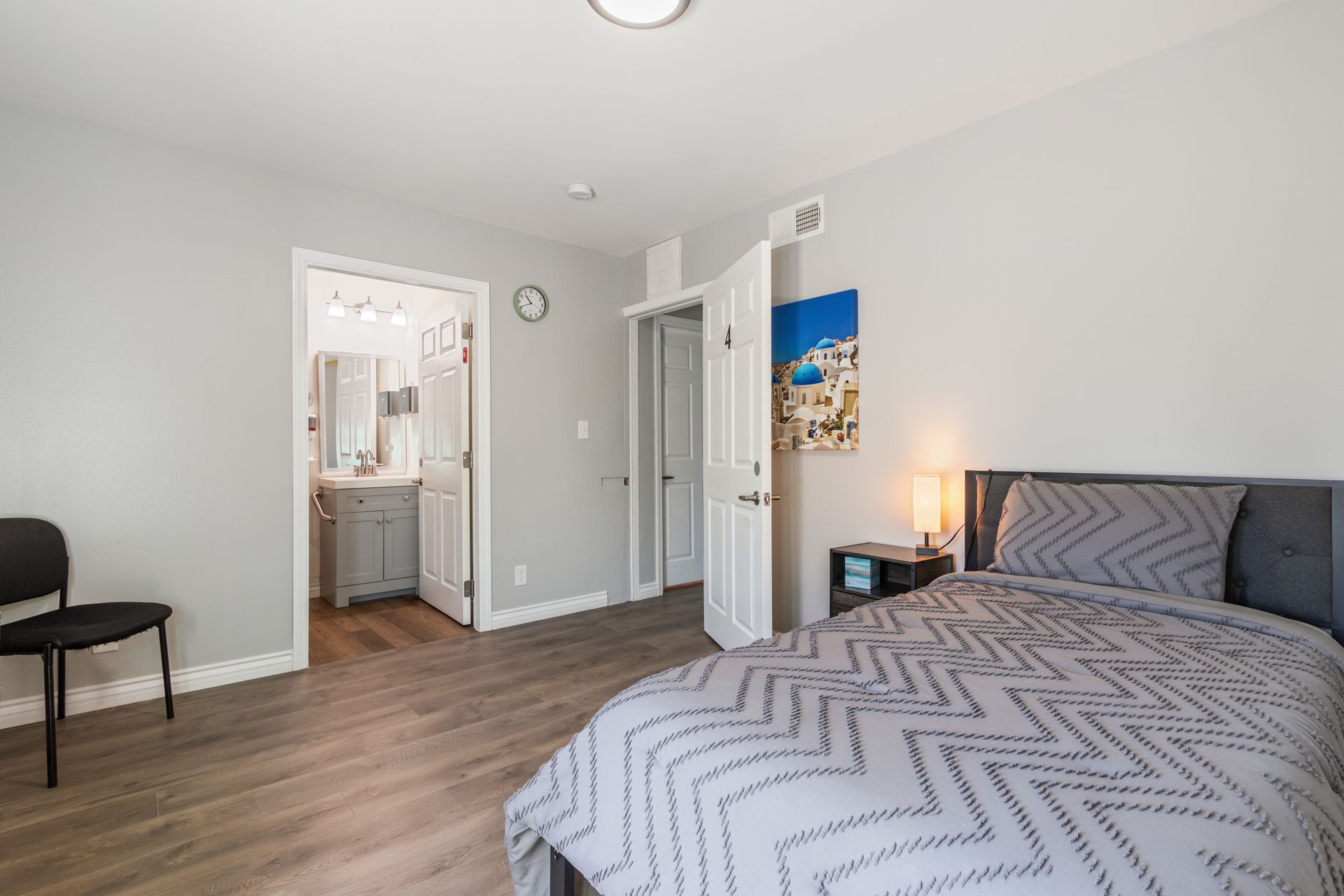 Bedroom with bed, door to bathroom, chair, painting, and hardwood flooring.