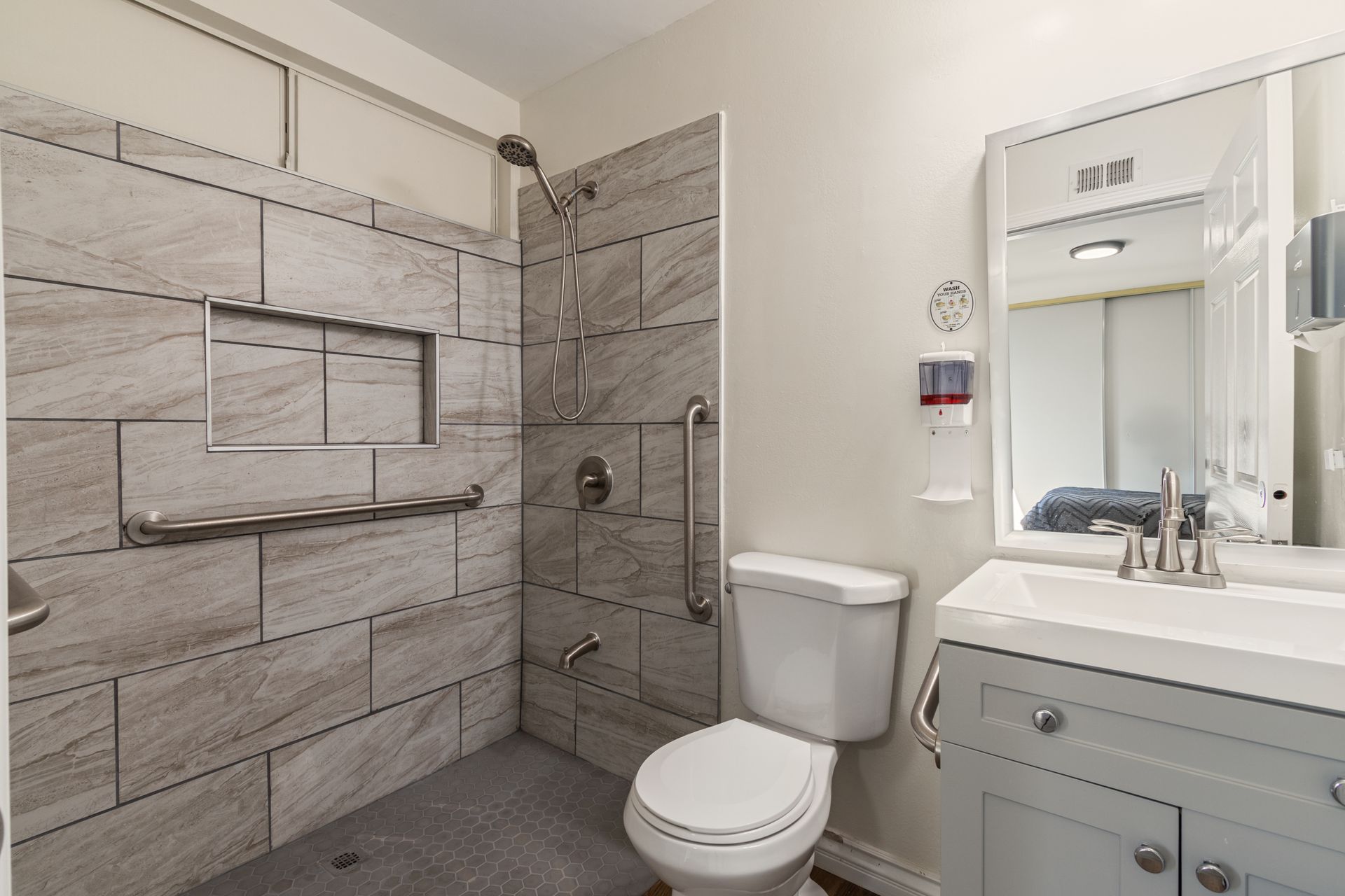 Accessible bathroom with gray tile shower, toilet, sink, and grab bars.