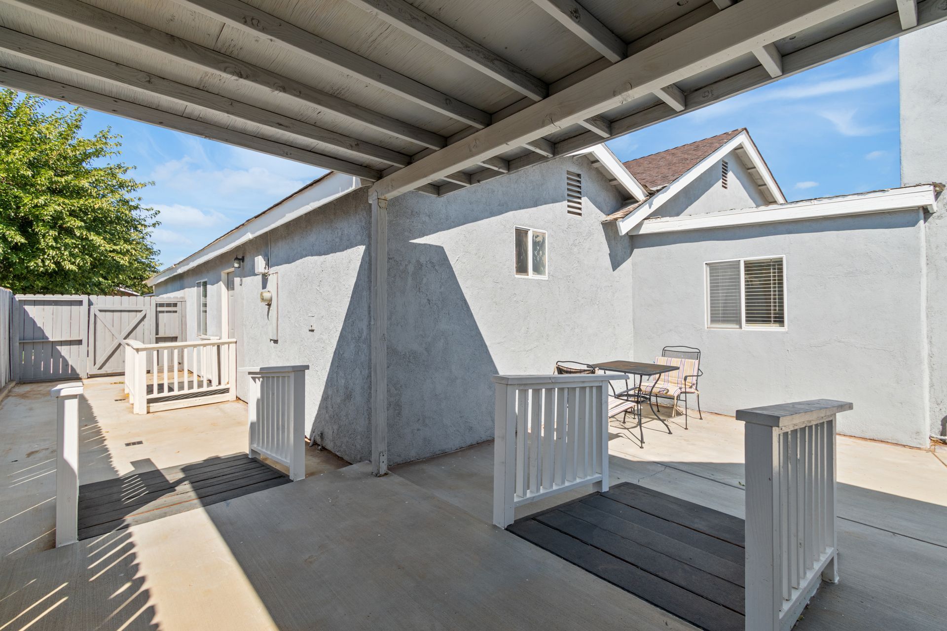 Patio with gray stucco walls, white railings, and a view of a house under a blue sky.