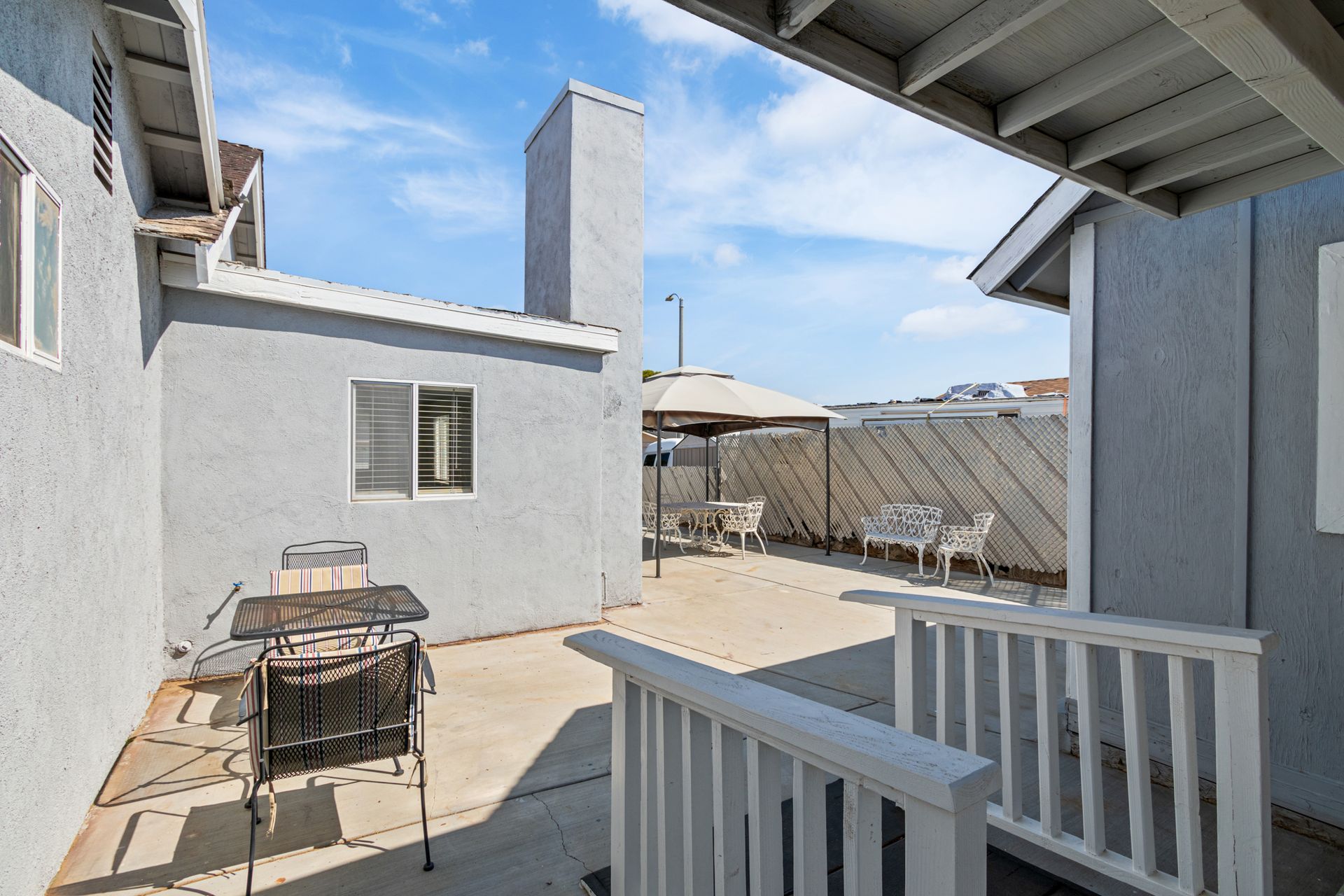 Gray patio with a grill, gazebo, and white railing under a blue sky.